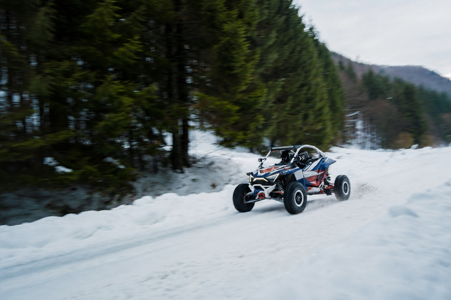 UTV with red white and blue high-tack graphics driving through winter off-road conditions